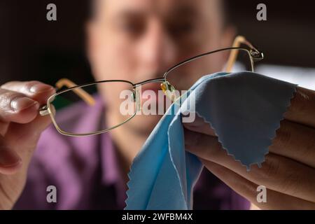 Pulizia degli occhiali. Un uomo gli asciuga gli occhiali con un panno. Messa a fuoco selettiva Foto Stock