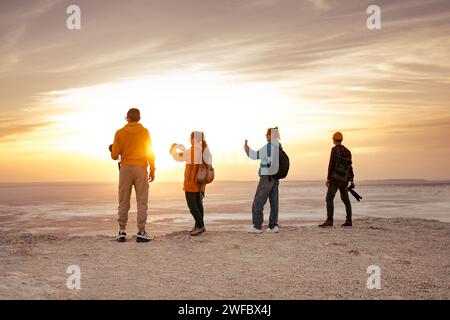 Quattro giovani escursionisti e fotografi con zaini sono in piedi al punto panoramico del tramonto e scattano foto Foto Stock