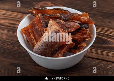 Pezzi di pesce secco pulito isolati su fondo di legno. Pollack piccante secco. Ambrato con pepe. Foto Stock