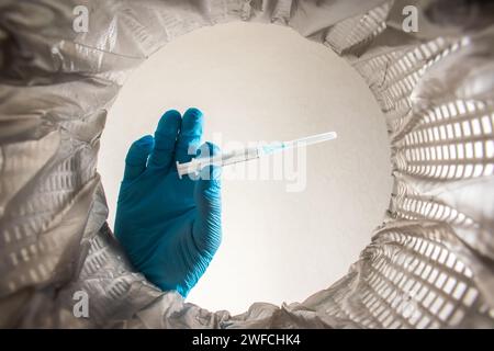 riciclaggio, smistamento dei rifiuti e concetto di sostenibilità - medico o operatore sanitario in guanti che gettano siringhe usate nella spazzatura. Foto Stock