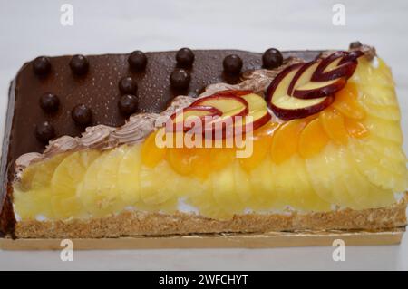 Torta di compleanno composta da due metà diversi pezzi, torta cremosa spugnosa per le celebrazioni, cioccolato fondente, caramello, panna alla vaniglia montata, fette di ananas Foto Stock