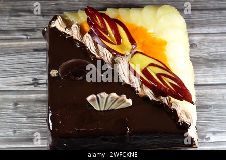 Torta di compleanno composta da due metà diversi pezzi, torta cremosa spugnosa per le celebrazioni, cioccolato fondente, caramello, panna alla vaniglia montata, fette di ananas Foto Stock