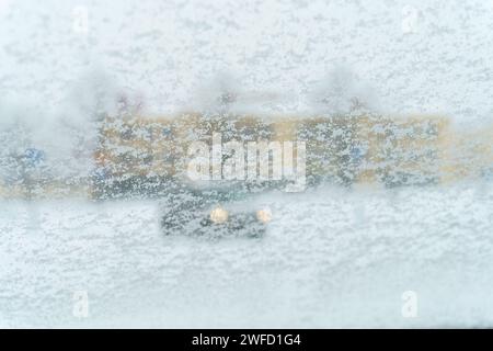 Parabrezza coperto di neve con edificio sfocato e un'auto sullo sfondo Foto Stock