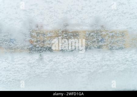 Parabrezza dell'auto coperto di neve con edificio sfocato sullo sfondo Foto Stock