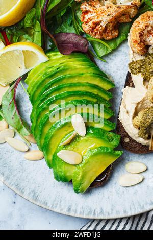 Brindisi vegani con avocado e cavolfiore alla griglia e pesto, sfondo in marmo grigio, vista dall'alto. Sana colazione a base di piante. Foto Stock