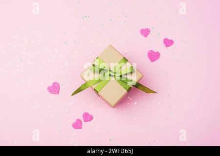 Confezione regalo con nastro verde, cuori rosa e decorazioni di coriandoli. Concetto di San Valentino. Vista dall'alto, base piatta. Foto Stock