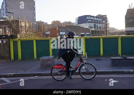 Un ciclista fa un viaggio su una bici Santander ad Hackney al primo mattino del sole invernale. Foto Stock