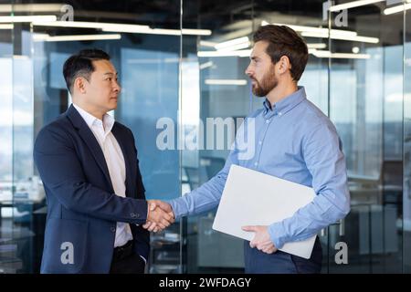 Due uomini d'affari professionisti si stringono la mano in un ambiente aziendale, a significare accordo, collaborazione e lavoro di squadra. Foto Stock