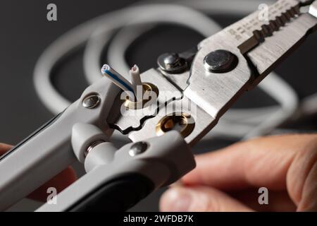 Un elettricista che indossa guanti da lavoro grigi sta spelando i fili elettrici con uno spelafili Foto Stock