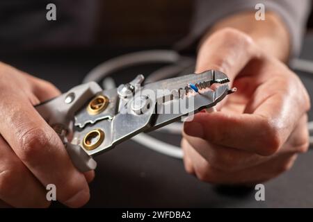 Un elettricista che indossa guanti da lavoro grigi sta spelando i fili elettrici con uno spelafili Foto Stock