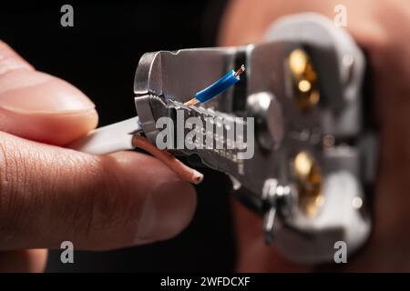 Un elettricista che indossa guanti da lavoro grigi sta spelando i fili elettrici con uno spelafili Foto Stock