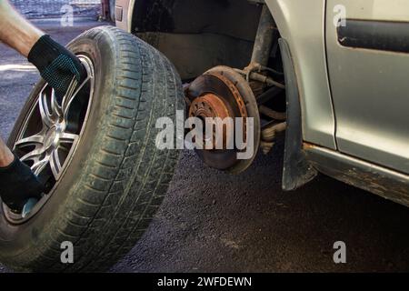 Riparazioni auto. Sostituzione delle ruote. Sostituzione stagionale degli pneumatici. Il master rimuove la ruota con entrambe le mani con la chiave. Un maestro in uniforme Foto Stock