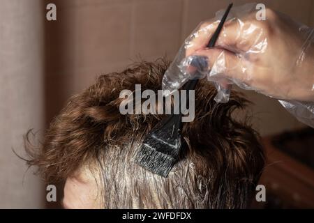 Closeup donna mani tintura capelli con una spazzola nera. Colorare i capelli bianchi a casa Foto Stock