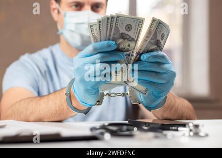 Un medico con banconote in dollari e manette. concetto di corruzione medica, corruzione, crimine. Foto Stock