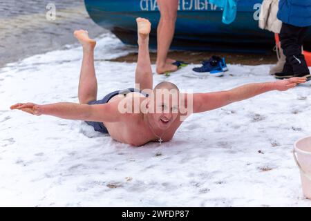 Grodno, Bielorussia - 28 gennaio 2024: Un uomo felice con le mutande giace sulla neve sulla riva del fiume durante la tradizionale gara annuale del temper-fest. A Foto Stock