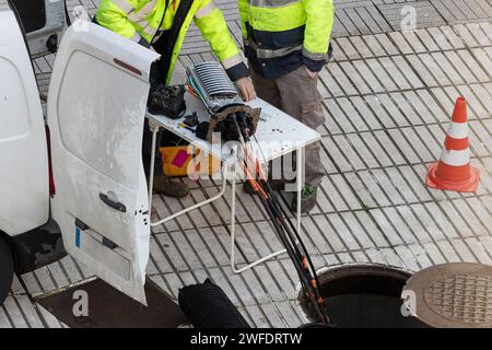 Tecnici addetti alla riparazione di linee di cavi in fibra ottica e al controllo su una strada cittadina Foto Stock