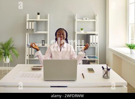 Giovane donna afroamericana lavoratrice d'ufficio che fa meditazione per ridurre lo stress sul lavoro Foto Stock