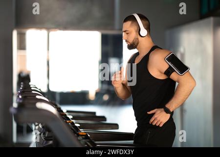 Bellissimo uomo maschile che indossa cuffie wireless in esecuzione sul tapis roulant in palestra Foto Stock