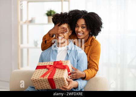 Una donna sorprende un uomo coprendo gli occhi da dietro mentre entrambi sorridono Foto Stock