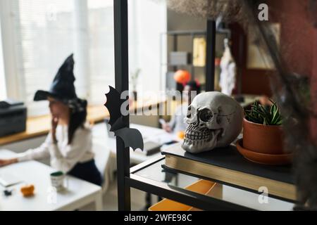 Teschio umano e vaso di fiori con pianta domestica verde in piedi sullo scaffale contro la giovane donna d'affari che indossa un cappello da strega Foto Stock