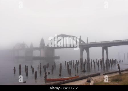 La nebbia mattutina copre il ponte Yaquina Bay a Newport, Oregon. La barca a file rosse si staglia oltre a putrefazione, armature in legno. Foto Stock