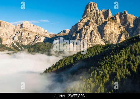 Il picco roccioso delle Alpi giganti sorge contro il cielo azzurro all'alba. La fitta nebbia avvolge le alte montagne in un'accattivante vista aerea in una soleggiata mattinata d'estate Foto Stock