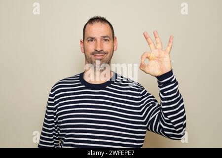 Ritratto di un allegro uomo ispanico che mostra un gesto ok isolato su sfondo beige. Foto Stock