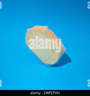 Fetta di pane bianco fresco con semi di sesamo avvolti in un foglio di alluminio su sfondo blu. Concetto di panetteria Foto Stock