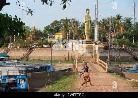 Il ragazzo attraversa il ponte con la statua del Buddha sullo sfondo nel villaggio galleggiante di Kampong Khleang, vicino a Siem Reap, Cambogia Foto Stock