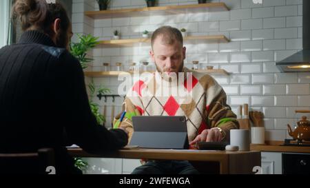 Due collaboratori freelance sono seduti nella cucina dell'ufficio a lavorare con un tablet, prendendo appunti in un luogo di lavoro moderno Foto Stock