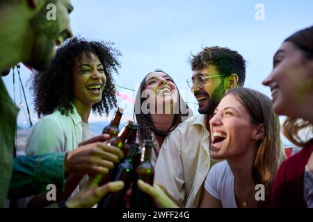 I giovani allegri e multirazziali brindano con delle bottiglie di birra che festeggiano le Risate estive all'aperto. Foto Stock
