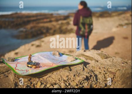 Attenzione selettiva su una vecchia bussola dorata d'epoca e mappa geografica sulla roccia su sfondo sfocato di una turista zaino che si gode il suo jour Foto Stock