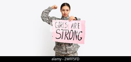 Giovane soldato che tiene in mano un poster con slogan LE RAGAZZE SONO FORTI su sfondo bianco. Concetto di femminismo Foto Stock