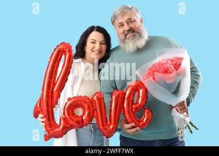 Bella coppia matura con bouquet di rose e palloncino a forma di AMORE PER le parole su sfondo blu. Festa di San Valentino Foto Stock