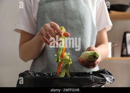 Donna che lancia bucce di verdure nel cestino della spazzatura in cucina, primo piano Foto Stock