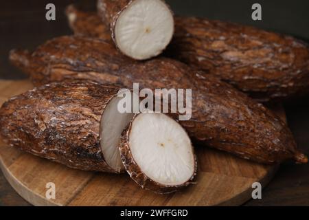 Radici di manioca intere e tagliate su tavola di legno, primo piano Foto Stock