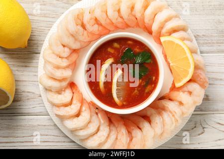 Gustosi gamberetti bolliti con salsa cocktail e limone su un tavolo di legno bianco, vista dall'alto Foto Stock