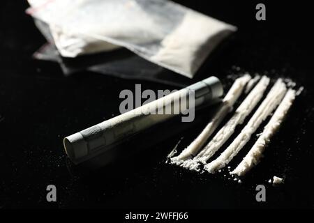 Tossicodipendenza. Cocaina e banconota da dollaro arrotolata sul tavolo nero, primo piano Foto Stock