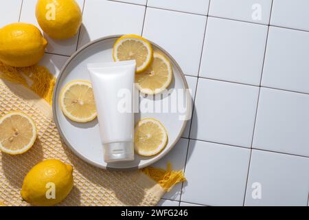 Una sciarpa di lana con un piatto di tubetto non etichettato e fette di limone. Spazio di copia sul lato destro. Sfondo tessere mosaico bianco. Limone (Citrus l Foto Stock