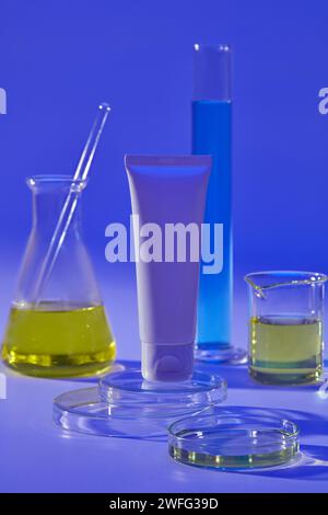 Laboratorio riempito di liquido blu e giallo decorato con una provetta bianca in piedi su podio rotondo. Mockup di tubo cosmetico per la cura della pelle di bellezza del viso Foto Stock