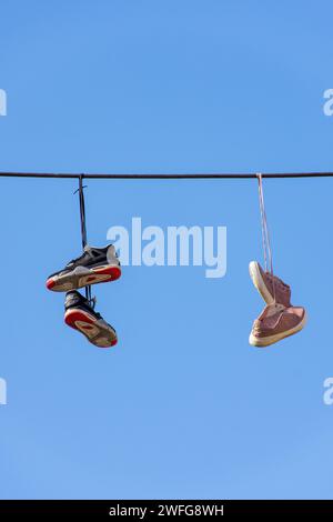 Vecchie scarpe da ginnastica appese su un cavo elettrico contro un cielo blu. Foto Stock