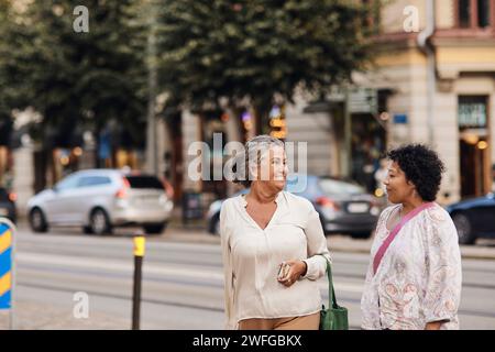 Donna disabile sorridente che parla con un'amica mentre si trova in strada in città Foto Stock