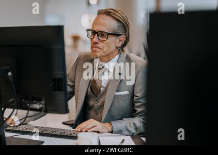 Uomo d'affari maturo che indossa occhiali che usa il computer alla scrivania in ufficio Foto Stock