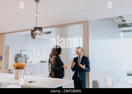 Un giovane uomo d'affari sorridente che discute con una donna d'affari anziana nel corridoio Foto Stock