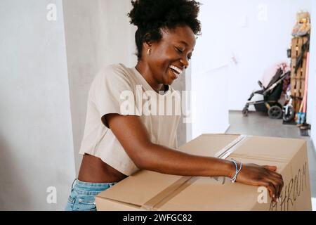 Una donna felice che tiene una scatola di cartone in una nuova casa Foto Stock