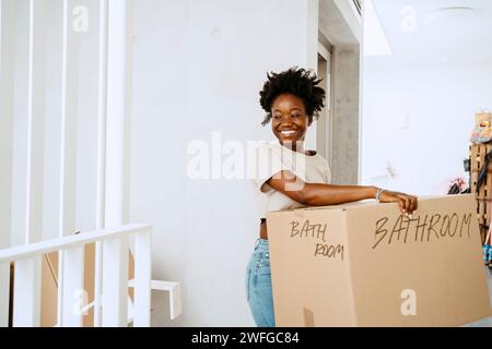 Donna sorridente che porta una scatola di cartone mentre si trova in una nuova casa Foto Stock