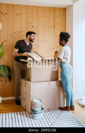 Accoppiare le scatole di disimballaggio mentre ci si trova vicino a un muro di legno nella nuova casa Foto Stock