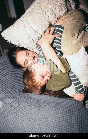 Vista dall'alto della donna felice che abbraccia il figlio mentre si sdraia a letto a casa Foto Stock