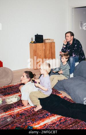 Bambini che giocano ai videogame mentre sono seduti con i genitori a casa Foto Stock
