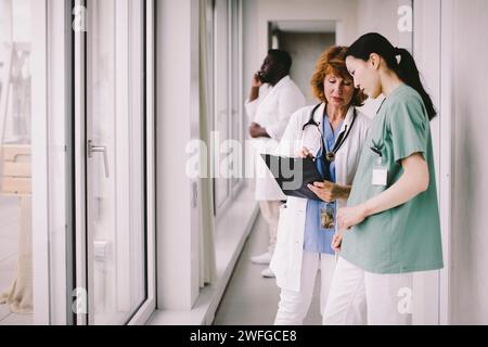 Medico donna anziana che discute sopra record con l'infermiera mentre si trova in corridoio dell'ospedale Foto Stock